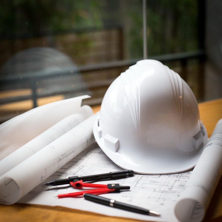 Casque de chantier et plans d’architecte posés sur des planches de bois